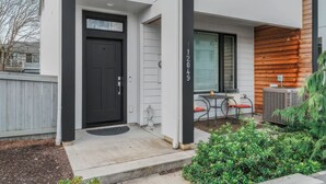 A modern building entrance with a black door, a small outdoor seating area, and a wooden wall. - Tranquil Townhome in Prime Location (Vancouver)