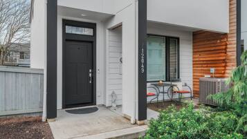 Une entrée moderne avec une porte noire, un petit espace extérieur aménagé en coin salon et un mur en bois.