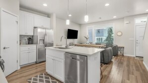 A modern kitchen with stainless steel appliances, a central island, and a dining area with a sofa. - Tranquil Townhome in Prime Location (Vancouver)