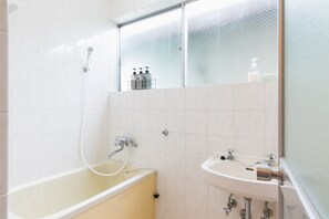 A bathroom with a bathtub, a sink, and a glass shower enclosure. - Naha Nishi EXseed (Naha)