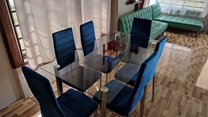 Et spiseområde med et glasbord og blå polstrede stole, en grøn sofa og en trægulv.