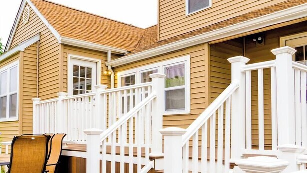 Una terraza de madera con una escalera blanca que conduce a un espacio cubierto con una mesa y sillas.