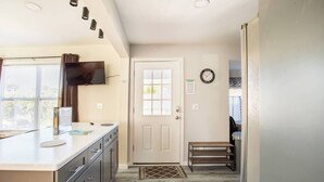 Una cocina compacta con una puerta blanca, un banco pequeño y un reloj en la pared.