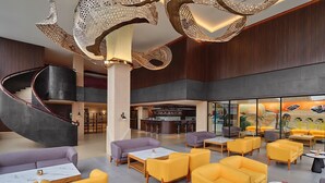 A spacious lobby with a central spiral staircase, yellow and purple seating areas, and a bar/lounge area with a mural. - Artotel Batam (Batam)