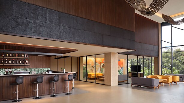 A modern bar area with a counter, stools, and a large window offering a view of greenery. - Artotel Batam (Batam)