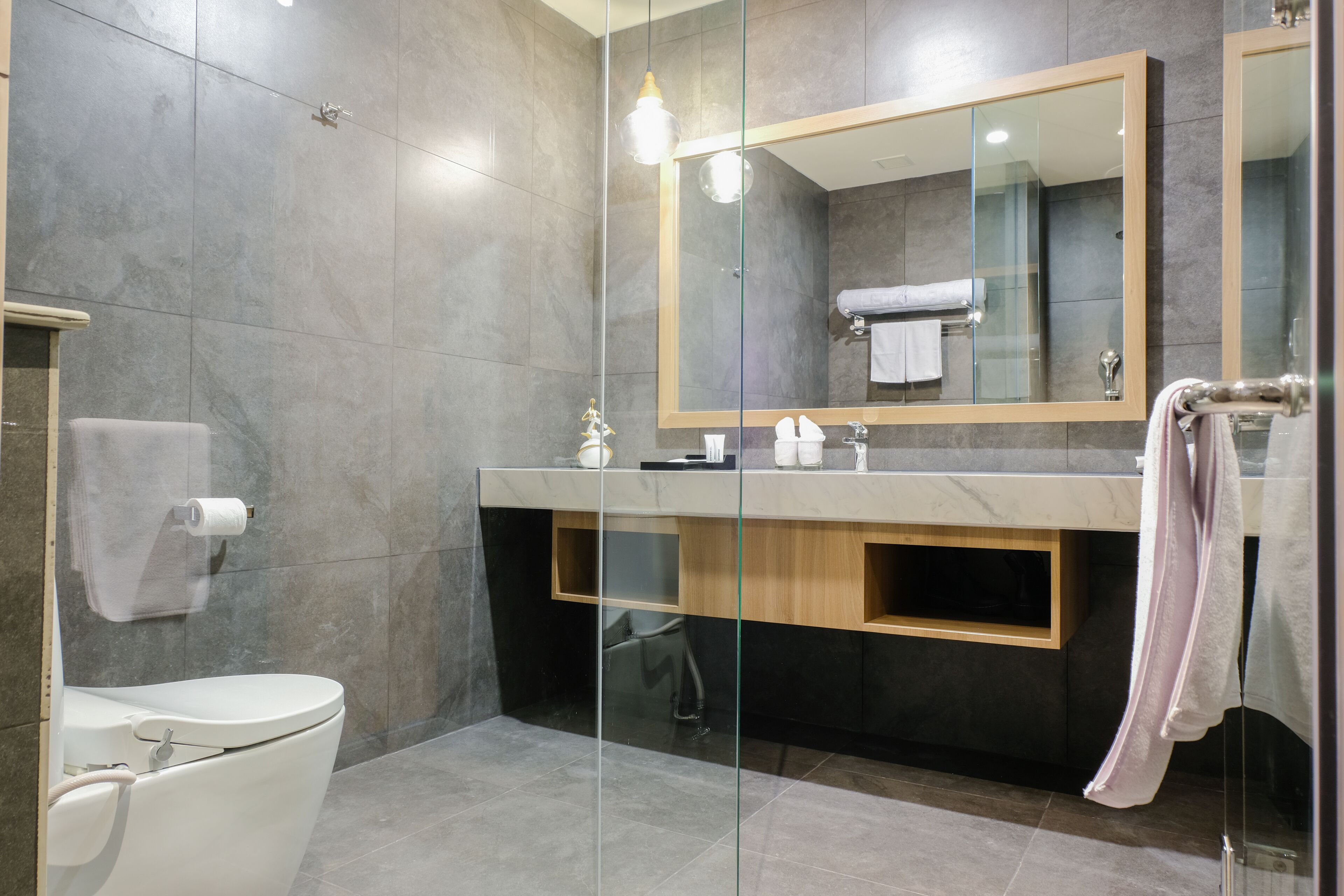 A modern bathroom with a glass shower enclosure, a toilet, a vanity with a mirror, and a towel rack.