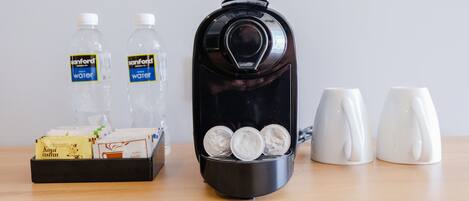 A coffee maker with three coffee cups, two bottles of water, and a tray with coffee pods and a box of instant coffee.