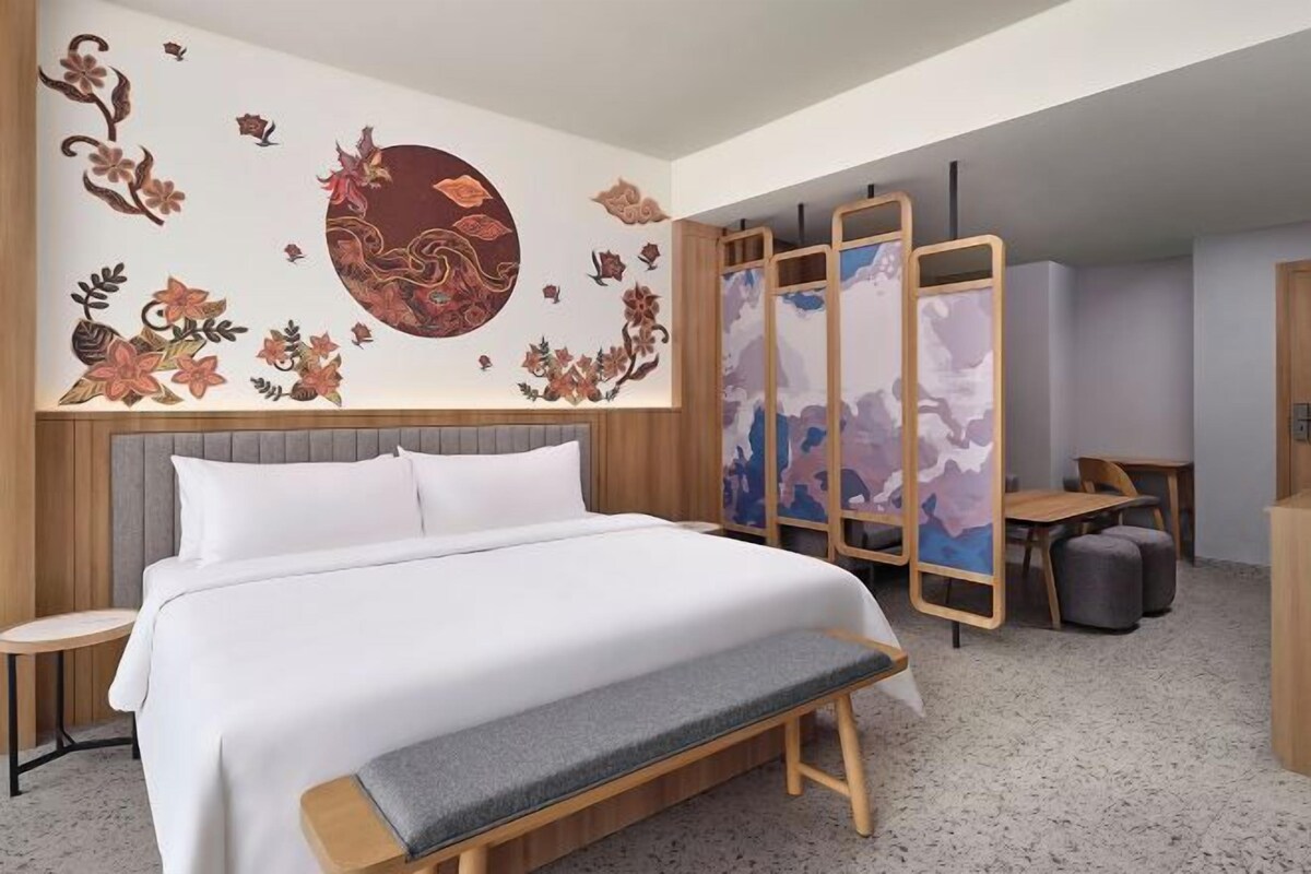 A modern hotel room with a large bed, a bench, a small table, and a decorative wall mural.