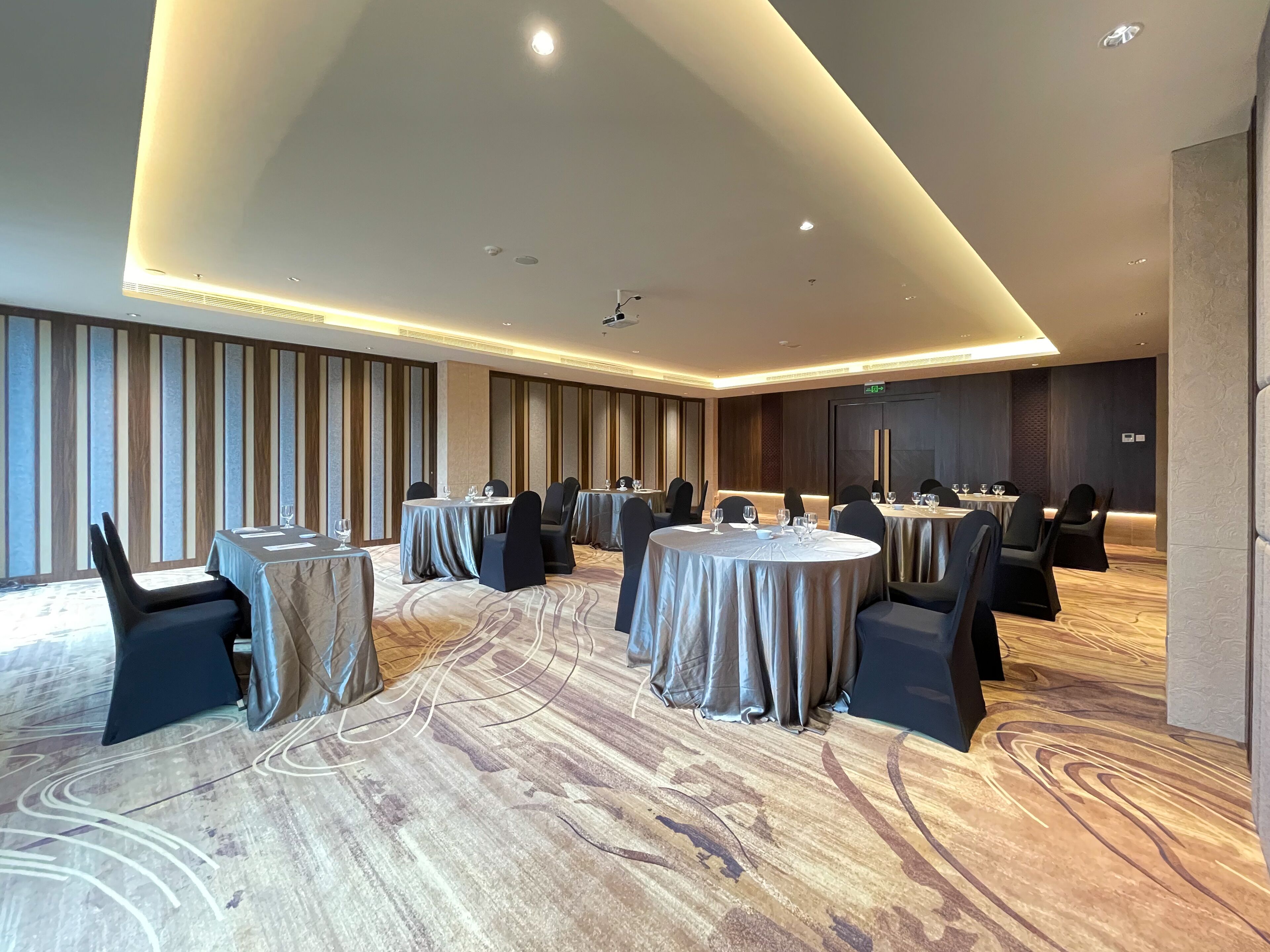Un salón de conferencias con mesas redondas, sillas negras y una alfombra estampada.