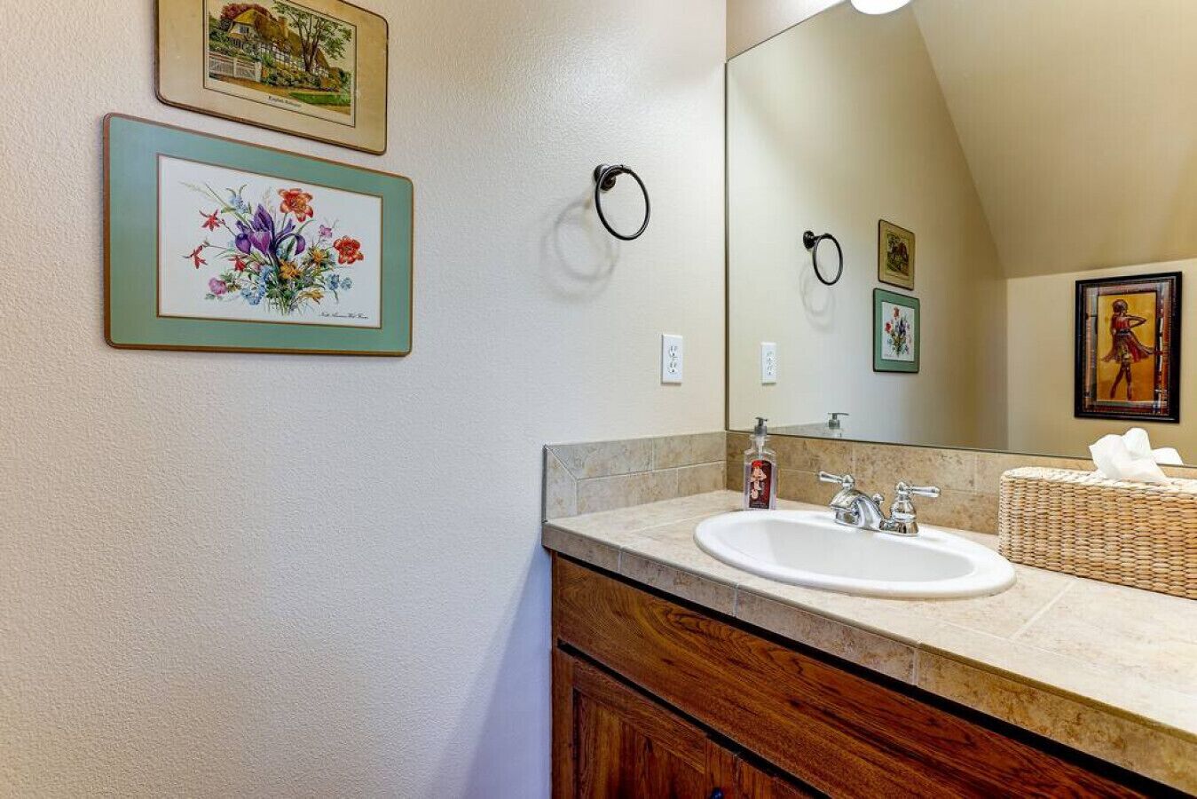 A bathroom with a sink, mirror, and framed floral artwork on the wall.