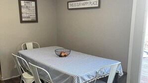 Un comedor con una mesa dispuesta para cuatro personas, sillas blancas, mantel a rayas y dos letreros en la pared.