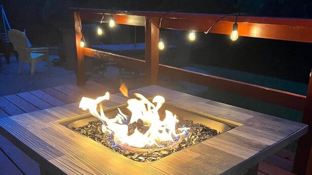 Un hogar cuadrado con estructura de madera y rejilla metálica, rodeado por una terraza de madera.