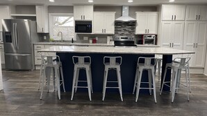 Una cocina moderna con armarios blancos, electrodomésticos de acero inoxidable y una isla central con taburetes de bar.