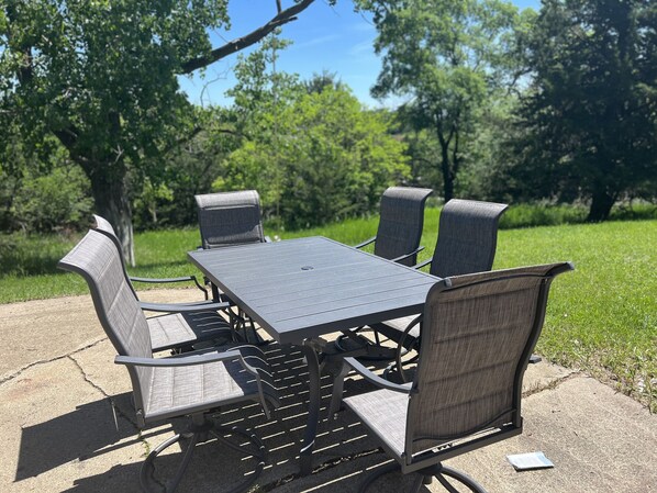 A square table with four chairs, set on a concrete surface in a park with trees in the background. - Haven by the Lake (Yankton)
