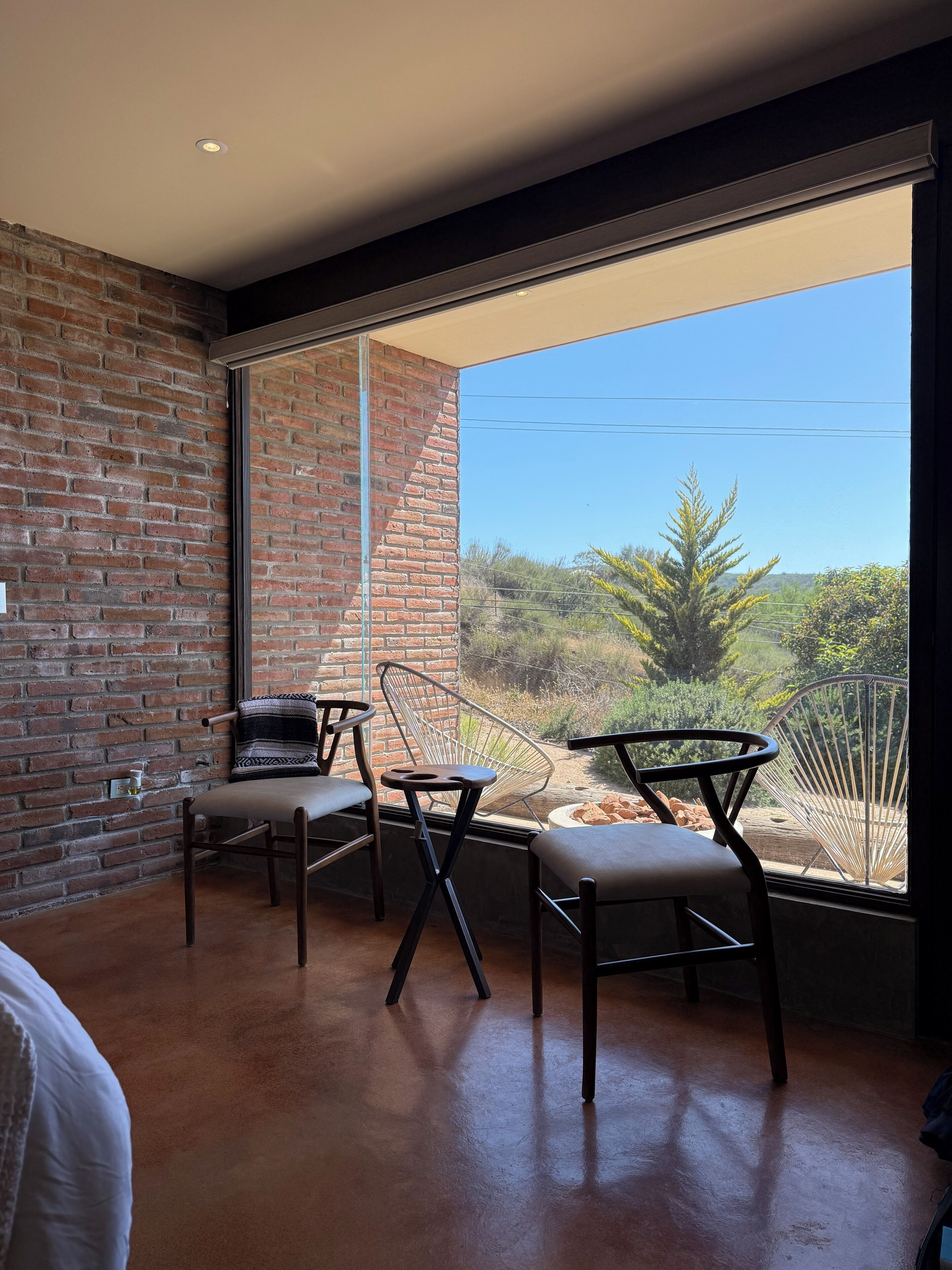 A modern room with a brick wall, large windows, and two chairs with cushions.
