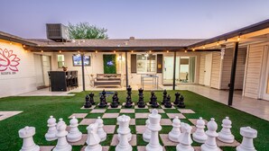 A spacious outdoor area with a large chessboard set up on artificial grass, a seating area with a sofa and table, and a building with a sign reading "BLISSFUL ZEN". - Zen home with heated swimming pool+ Billiards table+ arcade games (Scottsdale)