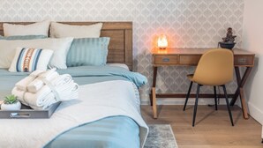 A neatly made bed with blue bedding, a wooden desk with a chair, and a nightstand with a lamp. - Zen home with heated swimming pool+ Billiards table+ arcade games (Scottsdale)