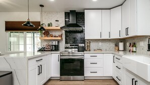 A modern kitchen with white cabinets, a stainless steel oven, and a black range hood. - Zen home with heated swimming pool+ Billiards table+ arcade games (Scottsdale)