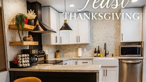 A modern kitchen with white cabinets, a wooden dining table with a box of donuts, and a baby seat. - Zen home with heated swimming pool+ Billiards table+ arcade games (Scottsdale)