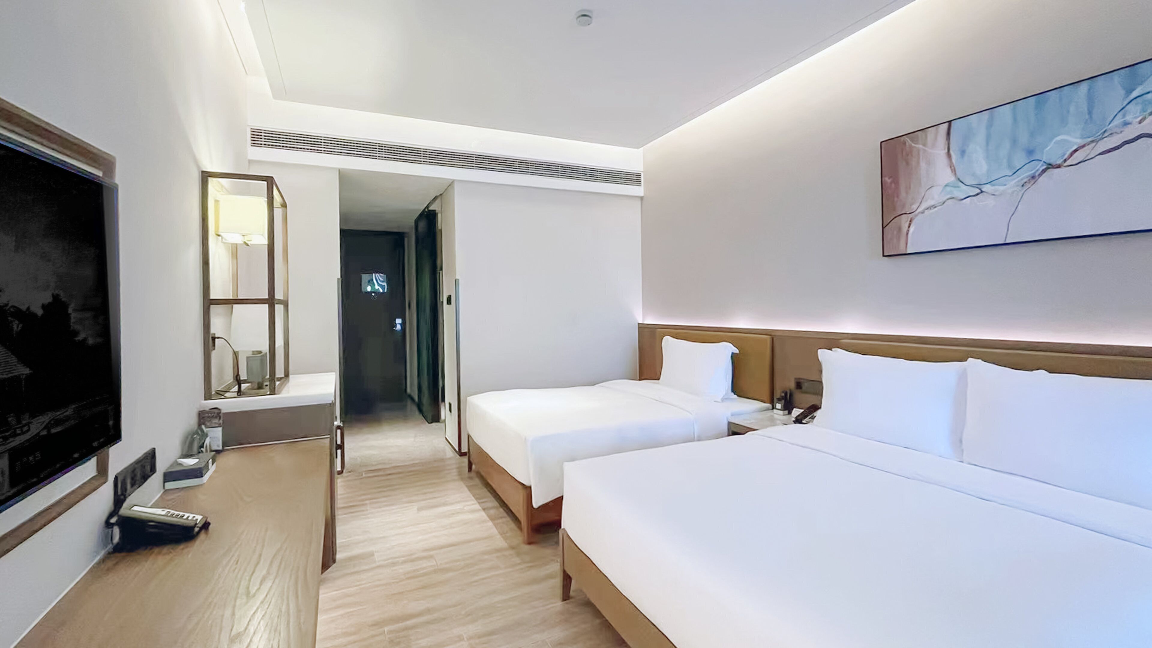 Ein Hotelzimmer mit zwei Betten, einem Fernseher, einem Gemälde und einem Flur, der in ein weiteres Zimmer führt.