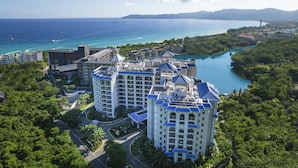Un hôtel de grande hauteur doté de nombreux balcons offrant une vue sur la côte, un port de plaisance avec des bateaux, et une vue dégagée sur l’océan.