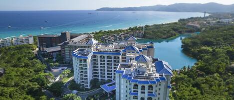 Un hotel moderno con numerosi balconi affacciati su una zona costiera, una marina con barche e una vista libera sull'oceano.
