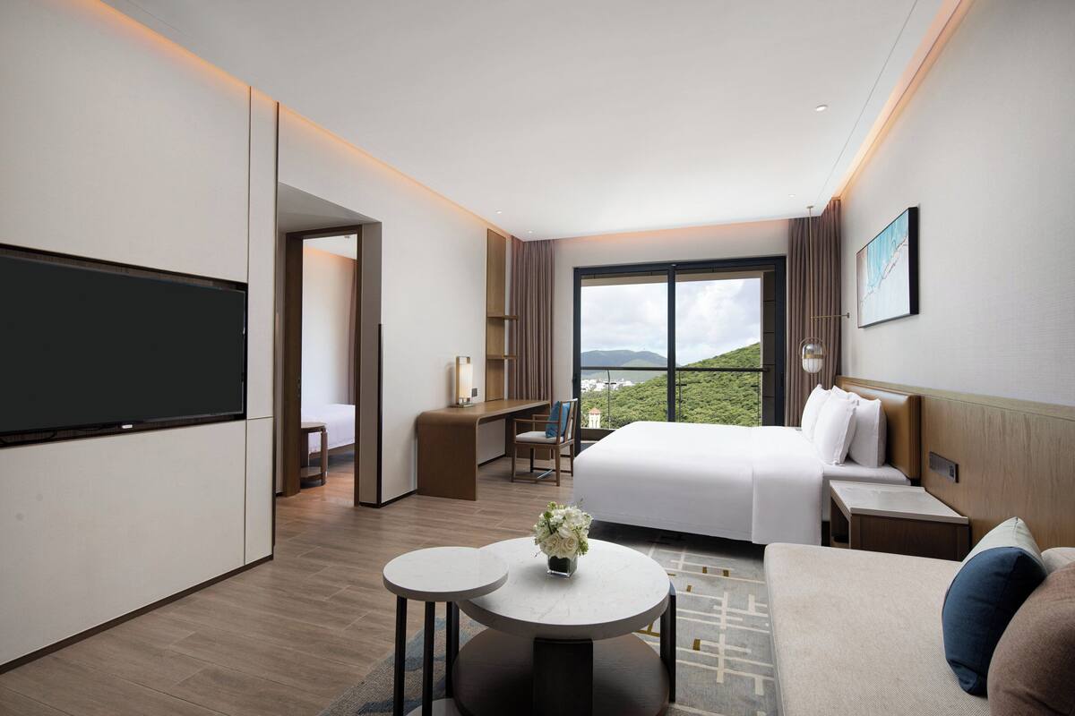 Een moderne hotelkamer met een groot bed, een bureau, een televisie en uitzicht op de omgeving.