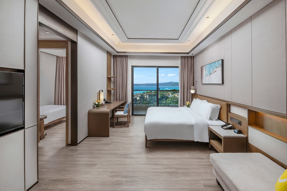 Une chambre d’hôtel comprenant un lit, des tables de chevet, une télévision, un bureau et une grande fenêtre donnant sur la ville.