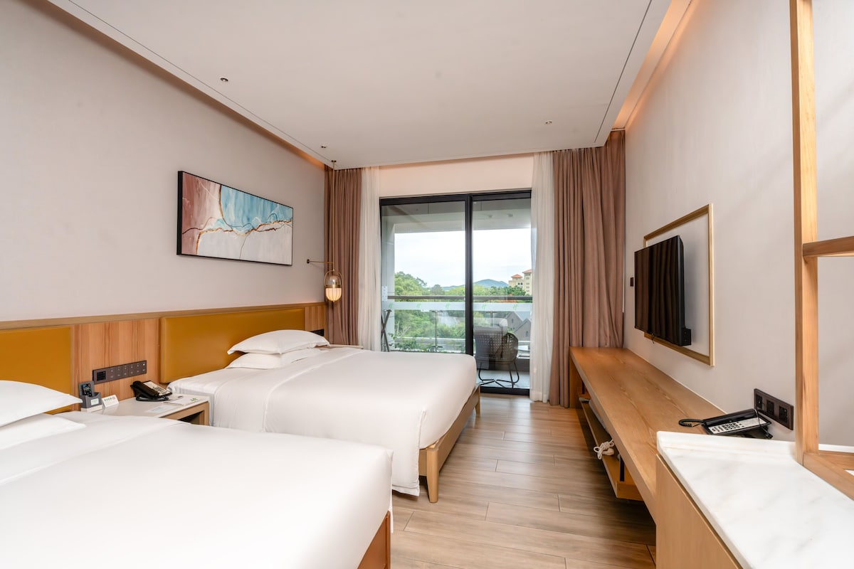 Ett hotellrum med två sängar, en TV, ett skrivbord, en telefon och ett fönster med utsikt.