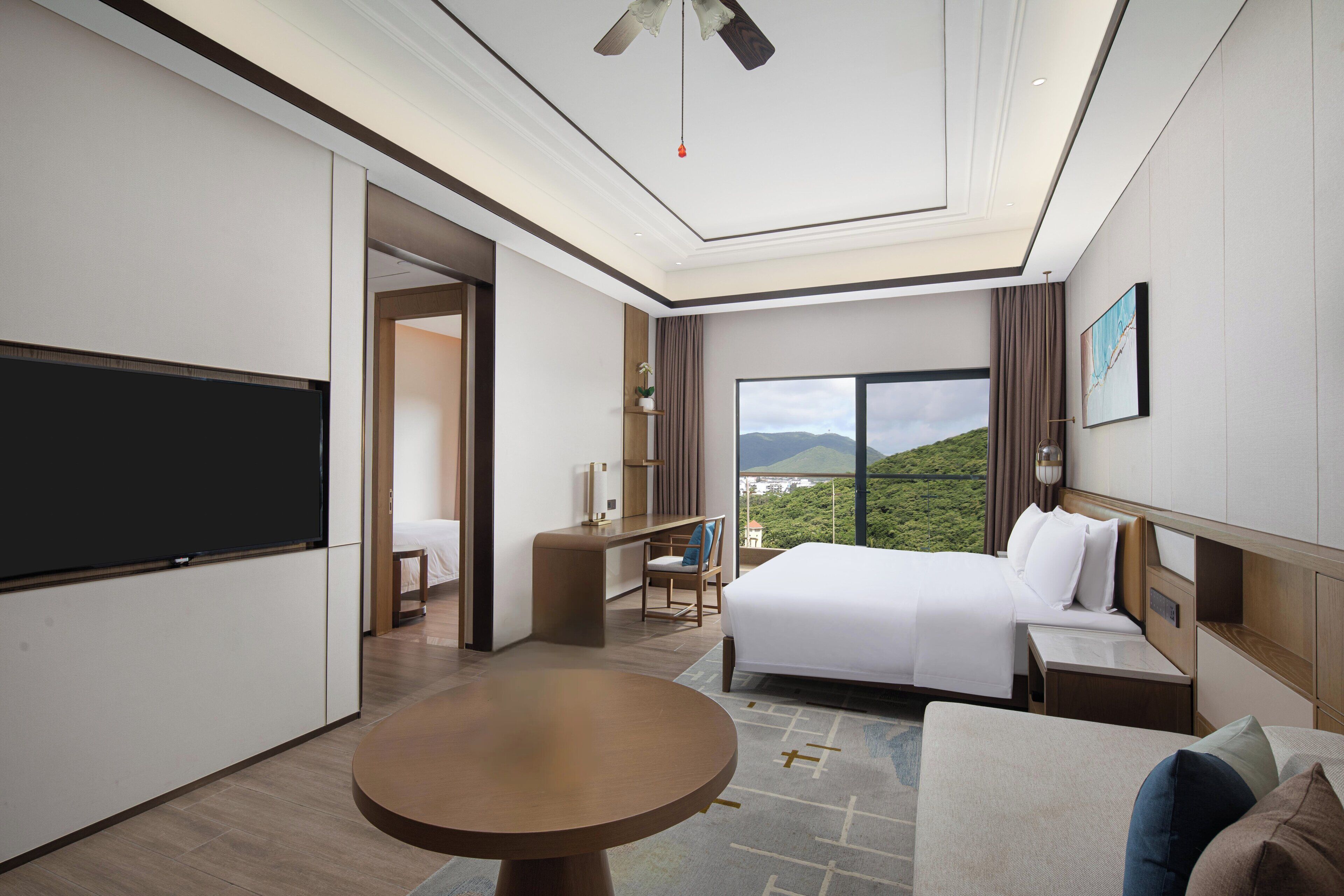 Ein modernes Hotelzimmer mit einem großen Bett, einem Schreibtisch, einem Fernseher und Blick ins Freie.