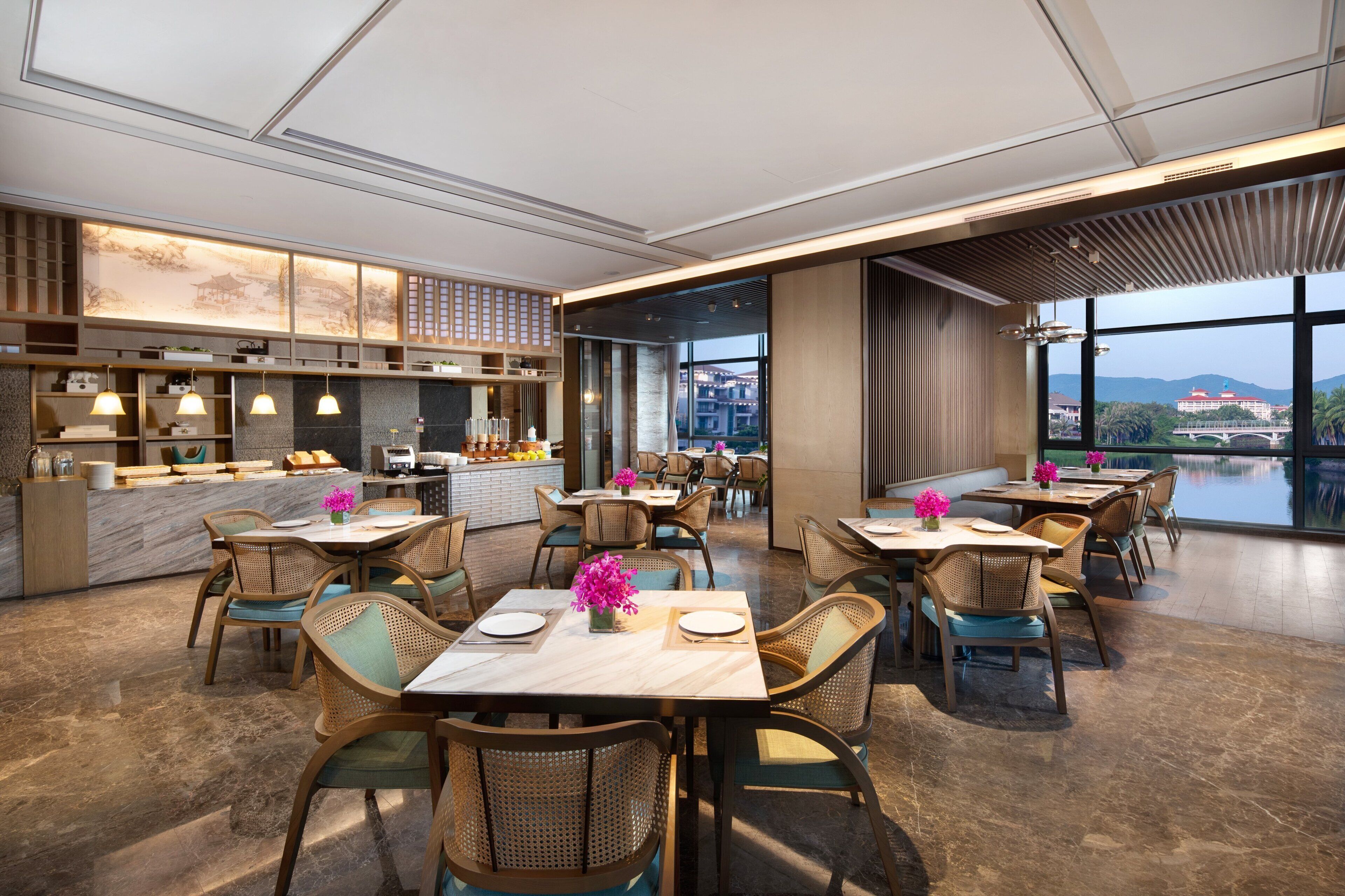A modern restaurant with a view of a bridge and mountains, featuring wooden furniture and a marble floor.