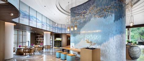 Un hall d’entrée spacieux avec un plafond haut, une grande fresque murale et un espace détente avec des tables et des chaises.