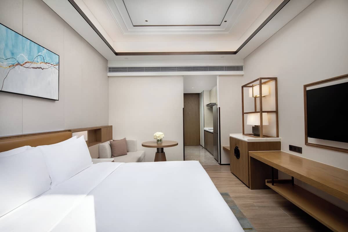 Una habitación de hotel moderna con una cama grande, una pequeña mesa redonda con un florero, un escritorio con una lámpara y un televisor en la pared.