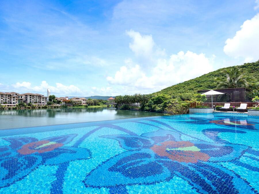 Una piscina con diseño en mosaico, rodeada de exuberante vegetación y un cielo despejado.