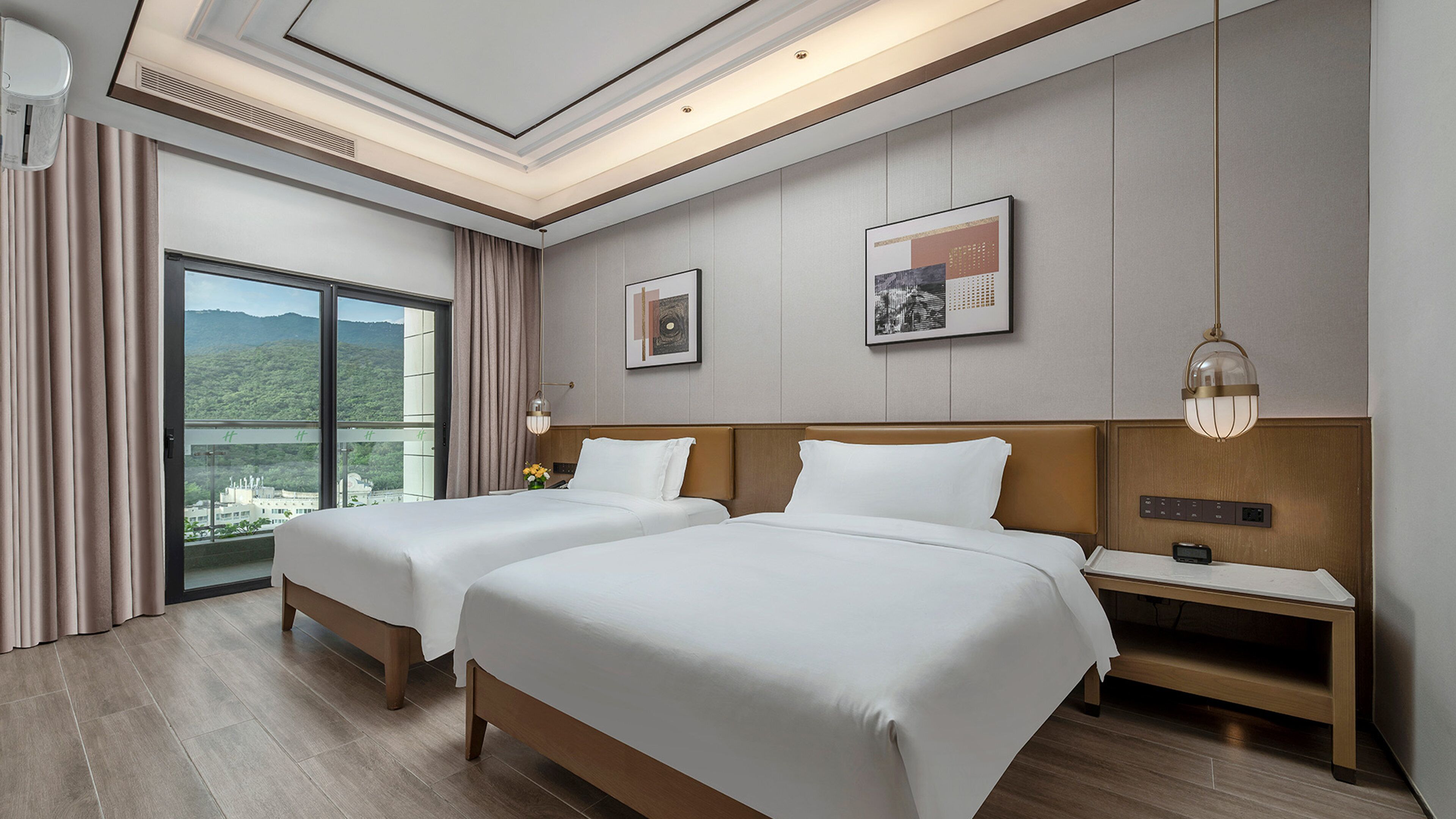 A hotel room with two beds, a large window with a view, a nightstand, and a wall-mounted lamp.