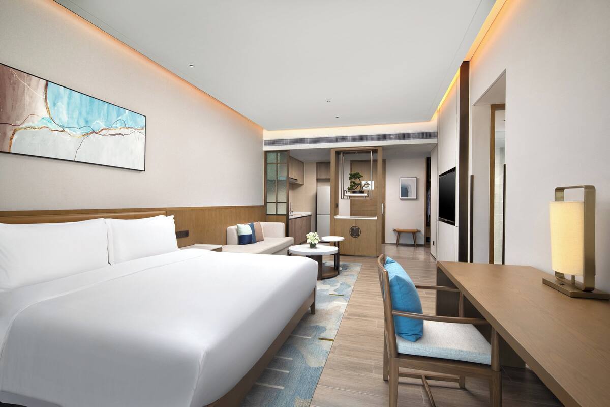 A hotel room with a large bed, a desk, a chair, a small table, and a TV.