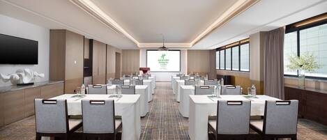 A conference room with multiple tables and chairs, a large screen at the front, and a patterned carpet.