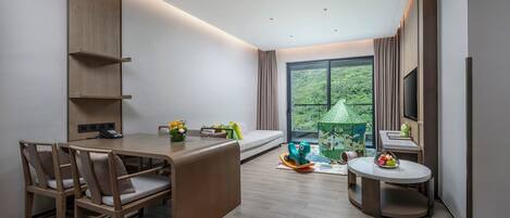 Una habitación de hotel moderna con comedor, sofá, una casita de juegos y un amplio ventanal con vistas a zonas verdes.