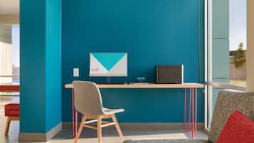A modern office space with teal walls, a wooden desk, a grey chair, and a red cushion.