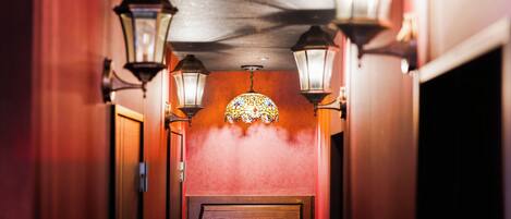 A hallway with a wooden door, two wall-mounted lanterns, and a stained glass window.