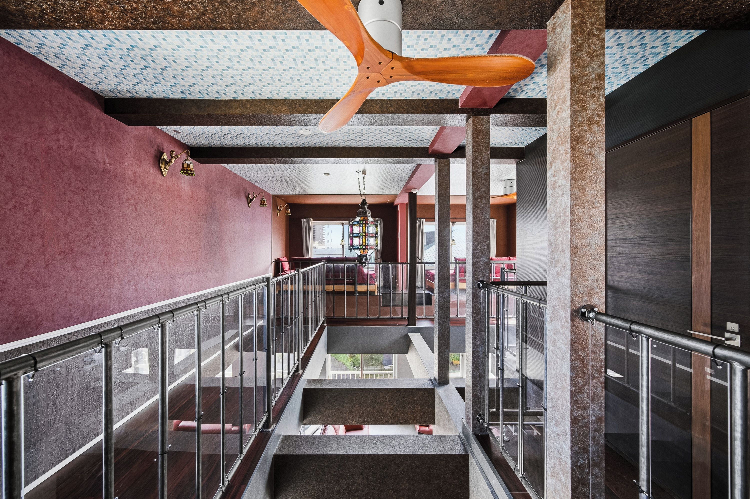 A hotel corridor with a glass railing, a ceiling fan, and a view of the lobby area.