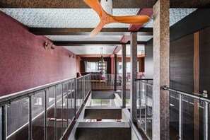A hotel corridor with a glass railing, a ceiling fan, and a view of the lobby area.