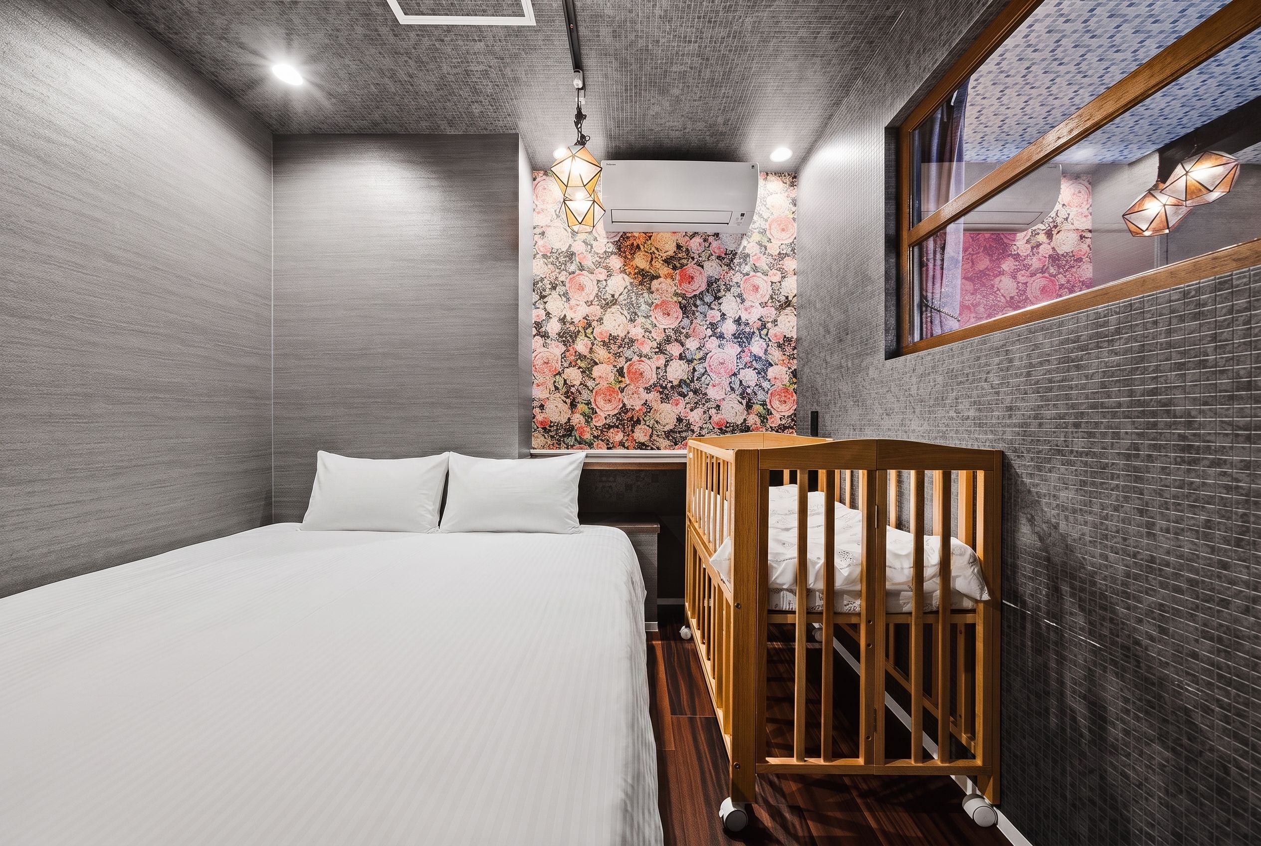 A bedroom with a bed, a crib, a mirror, and a floral wallpaper.