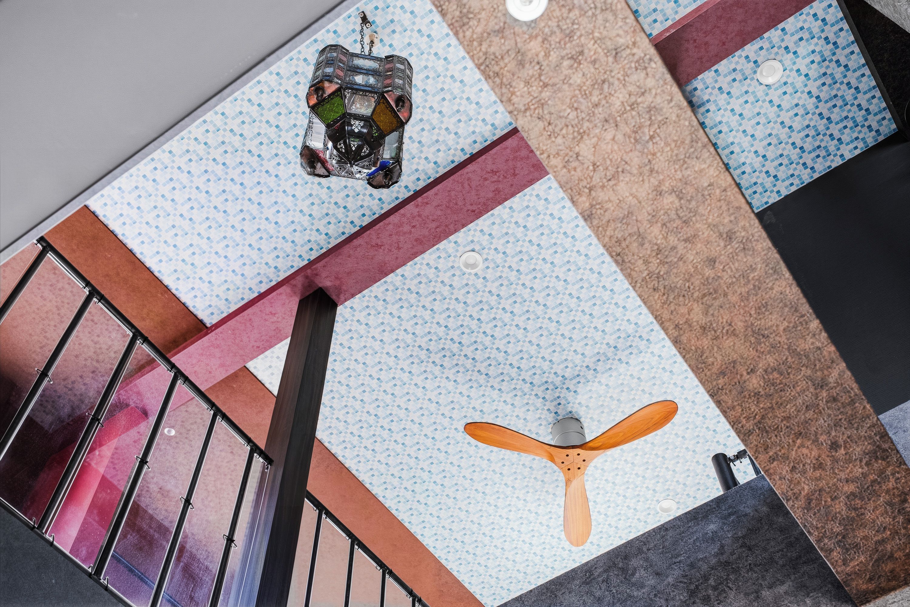 A modern interior with a geometric patterned floor, a wooden ceiling fan, and a metal railing.
