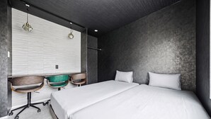 A modern bedroom with a large bed, two chairs, a desk, and a window with blinds. - THE BEEHIVE AIOI (Otaru)