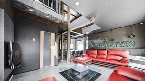 A modern living room with a sectional sofa, a glass coffee table, and a flat-screen TV. - THE BEEHIVE AIOI (Otaru)