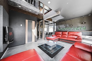 A modern living room with a sectional sofa, a glass coffee table, and a flat-screen TV. - THE BEEHIVE AIOI (Otaru)
