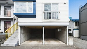 A two-story building with a covered parking area and a yellow staircase leading to the entrance. - THE BEEHIVE AIOI (Otaru)