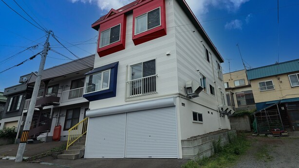 A multi-story residential building with a red roof, white walls, and a garage. - THE BEEHIVE AIOI (Otaru)