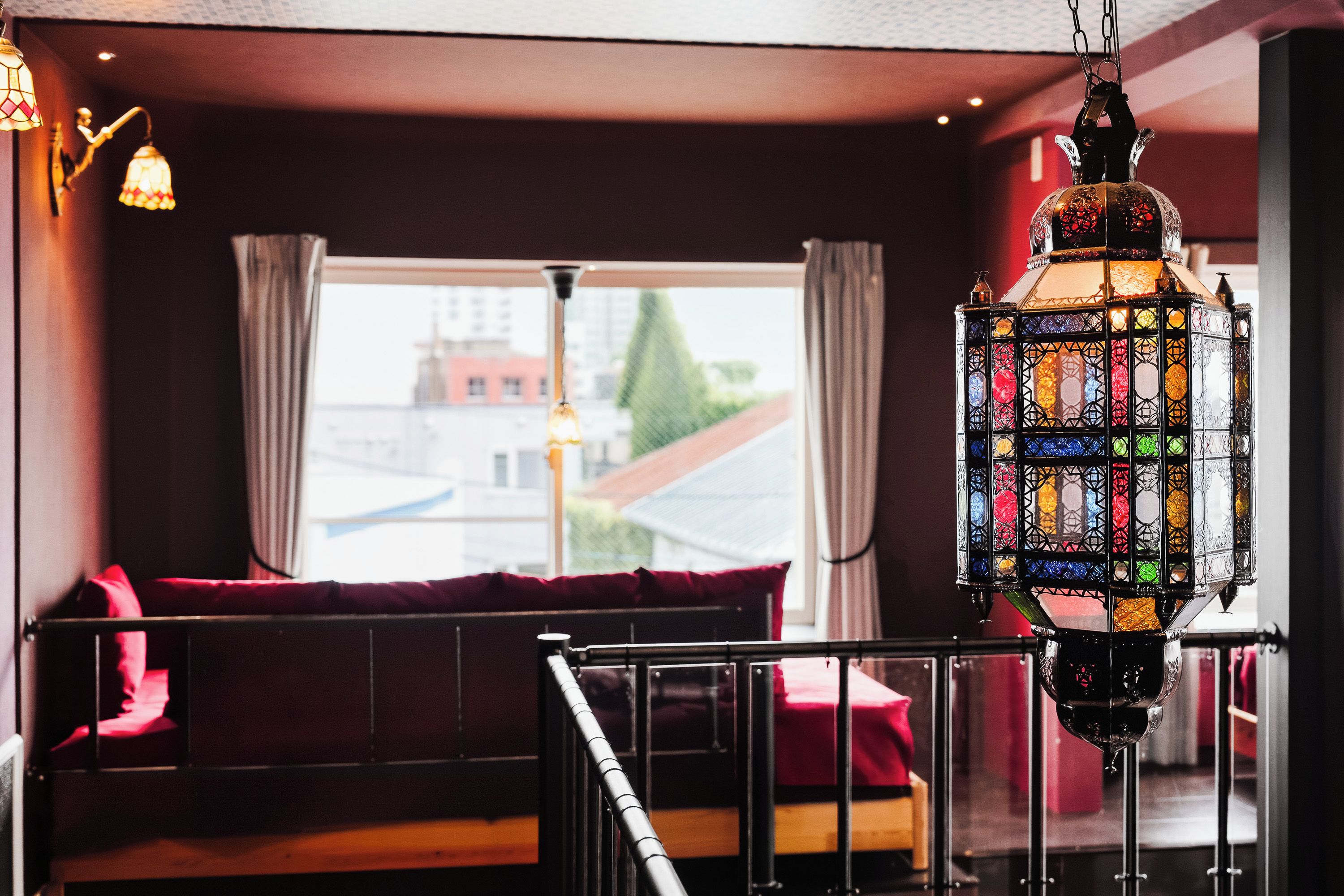 A room with a view of a building through a window, a hanging lantern, and a red sofa.